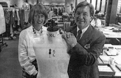 A nicely dressed man and a woman smile while standing near a clothing mannequin